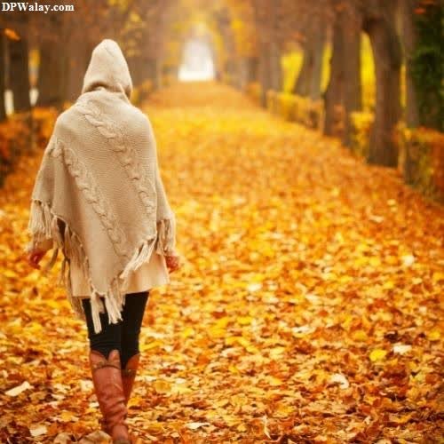 a woman walking down a path covered in autumn leaves