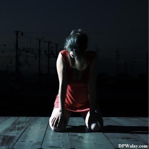 a woman sitting on a wooden floor in the dark 