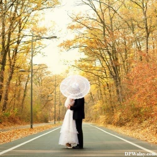 a bride and groom standing on the road in the fall