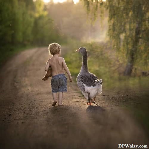 a boy walking down a dirt road with a goose