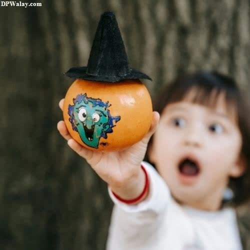 a little girl holding a pumpkin with a witch hat on it 