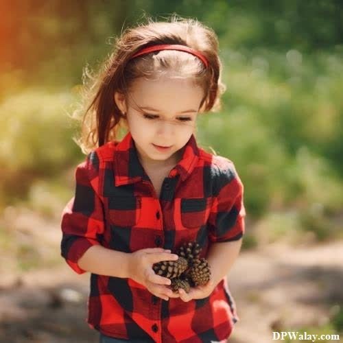 a little girl in a red and black shirt holding a pine cone 