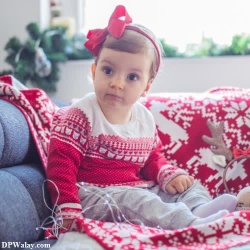 a baby girl sitting on a couch with a christmas sweater