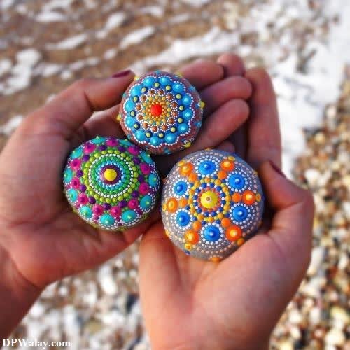 a person holding three colorful painted rocks