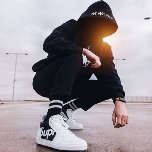 a man in a black hoodie and white sneakers crouching on the ground