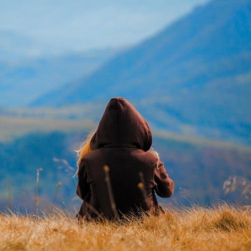 a person sitting in a field looking at the mountains 