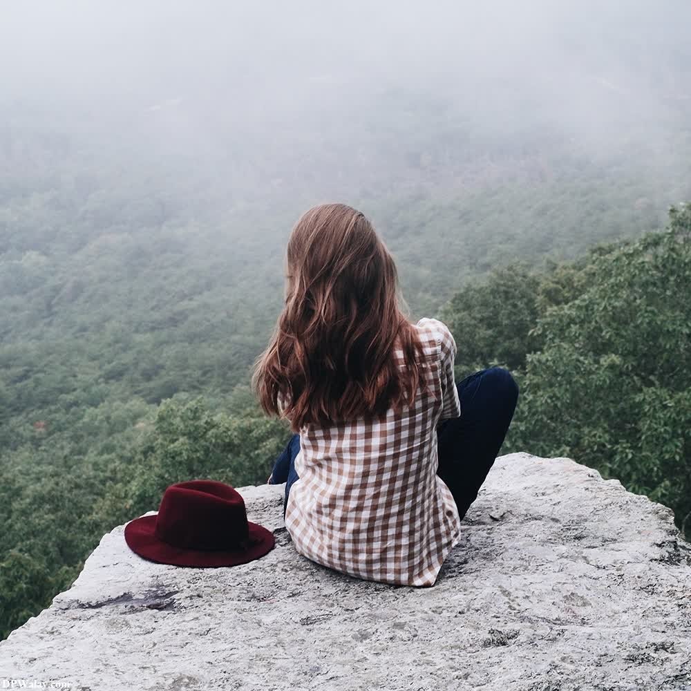 a woman sitting on top of a mountain looking out over the foggy hills