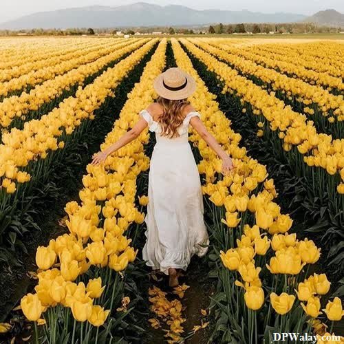 a woman in a white dress and hat walking through a field of yellow tulips 