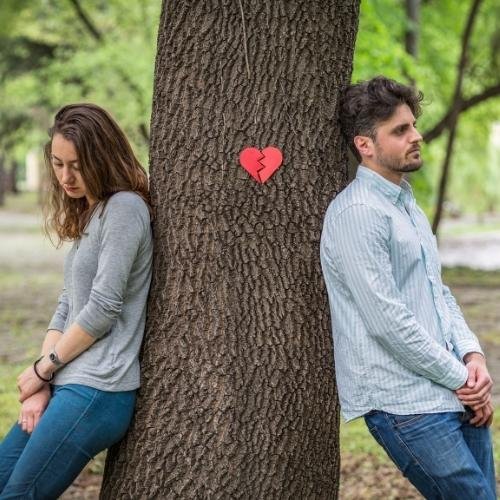 a couple sitting on the ground next to a tree 