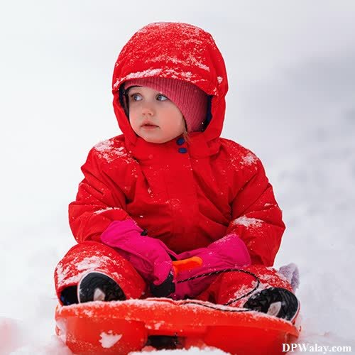 a little girl in a red coat and hat sitting on a sler
