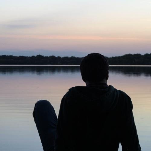 a man sitting on the edge of a lake looking out at the sunset images by DPwalay