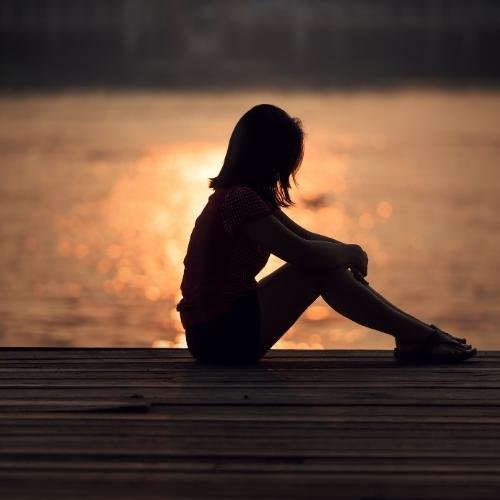 sad whatsapp dp - a woman sitting on a dock looking out at the water