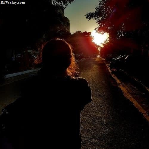 a woman walking down a street at sunset 