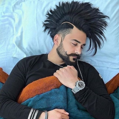 a man with a mohawk and a beard laying on a bed