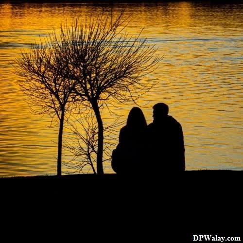 a couple sitting on the bank of a river at sunset