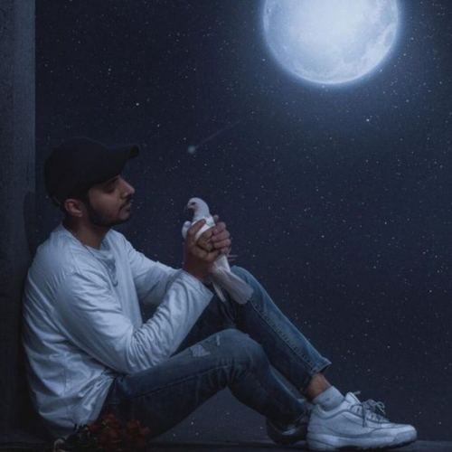a man sitting on the ground in front of a full moon