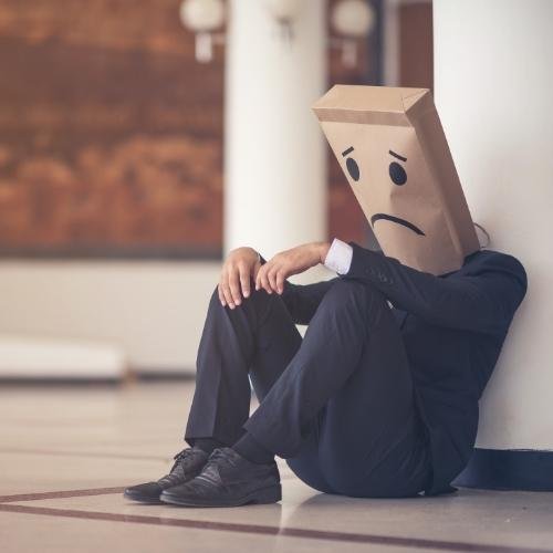 a man in a suit sitting on the floor with a cardboard box over his head