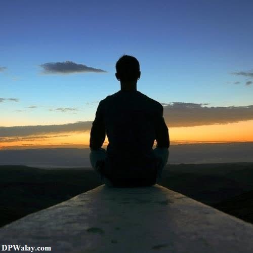 a man sitting on a ledge looking at the sunset 