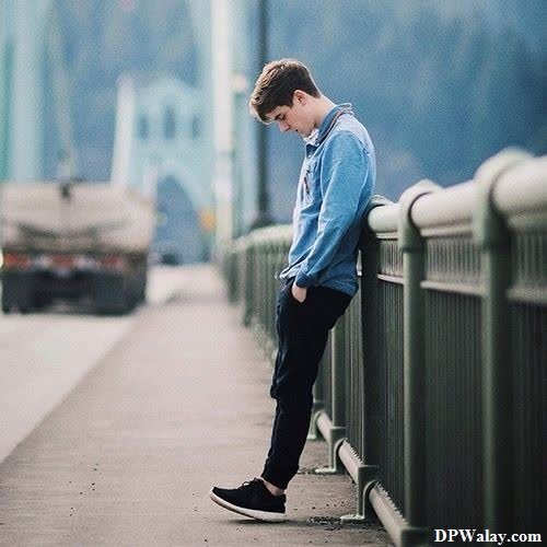 a boy sitting on a bridge looking down 