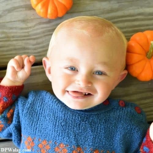 a baby in a blue sweater and orange pumpkins 