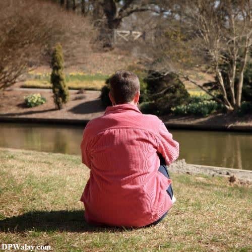 a man sitting on the grass near a pond