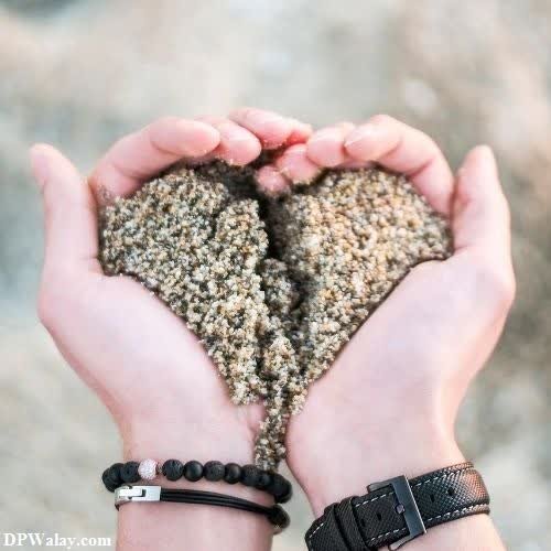 two hands holding sand hearts in the sand