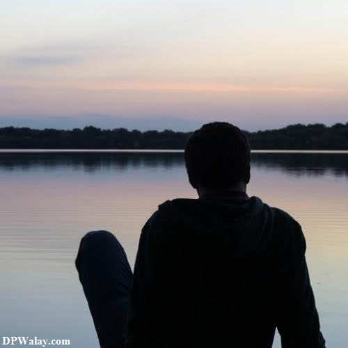 a man sitting on the edge of a lake looking out at the sunset