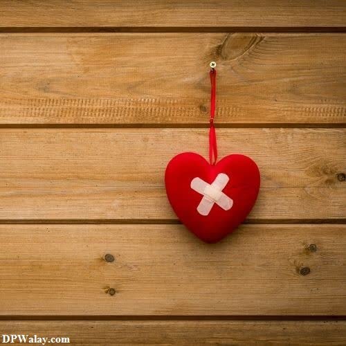 a red heart hanging on a wooden wall love breakup whatsapp dp