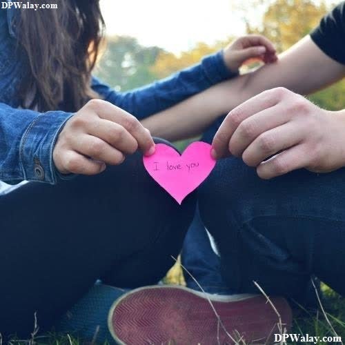 a couple sitting on the grass holding a pink heart love symbol images for whatsapp dp 