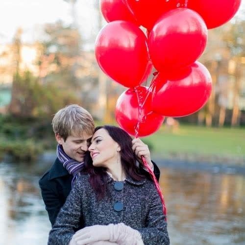 a couple holding red balloons in front of a lake