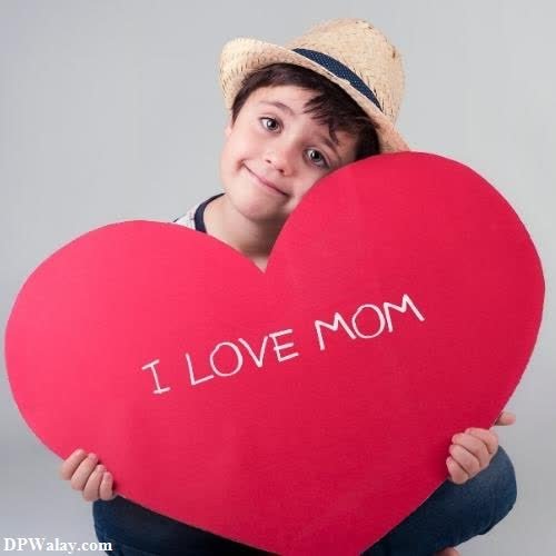 a young boy holding a heart shaped pillow with the word love mom