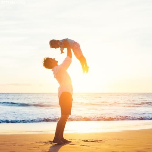 a woman holding a baby on the beach at sunset