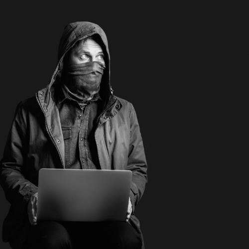 a man in a hoodie sits on a stool with his laptop