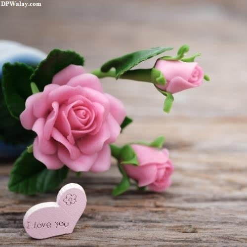 a pink rose and a small heart on a wooden table