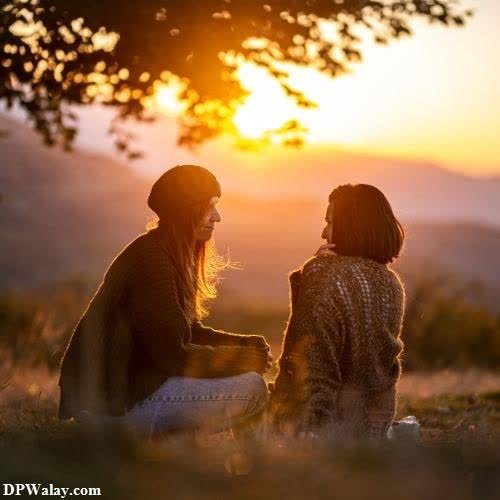 two women sitting in the grass at sunset 