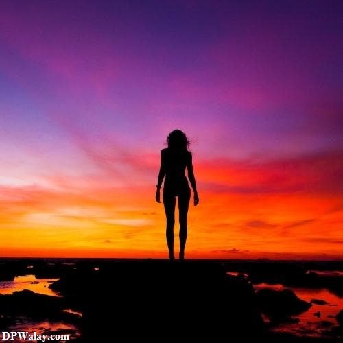 a woman standing on a rock at sunset