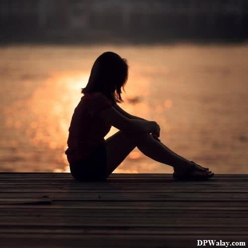a woman sitting on a dock looking at the sunset
