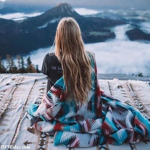 a woman sitting on a blanket looking out over the mountains