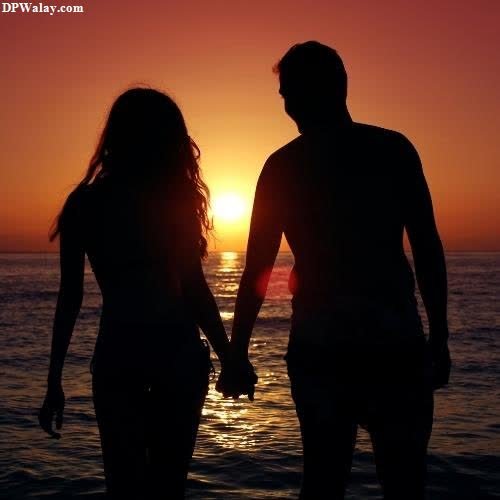 a couple holding hands and walking into the ocean at sunset 