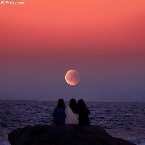 two people sitting on rocks looking at the moon