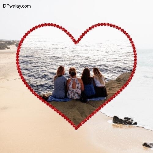 two girls sitting on the beach with a heart shaped frame