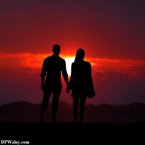 a couple holding hands as the sun sets behind them