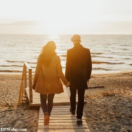 a couple walking down a wooden walkway towards the ocean