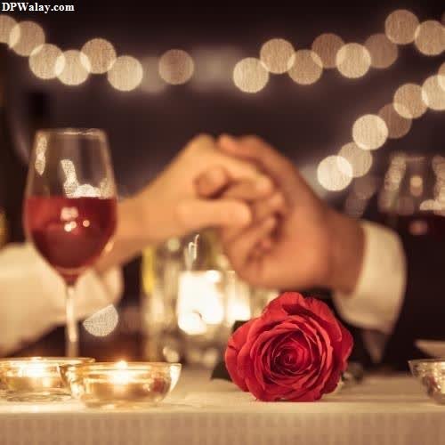 a couple holding hands at a table with candles and roses