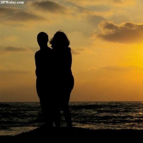 a couple standing on the beach at sunset