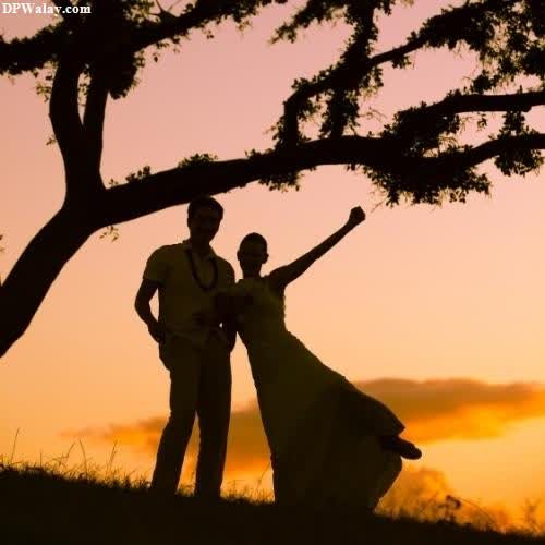 a bride and groom standing under a tree at sunset