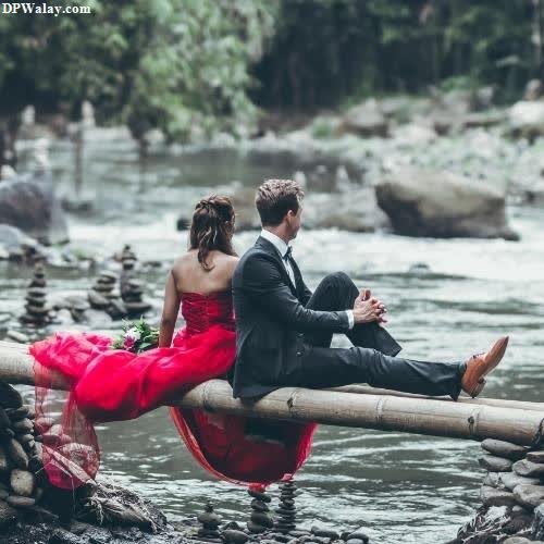 a couple sitting on a bamboo bridge in the middle of a river