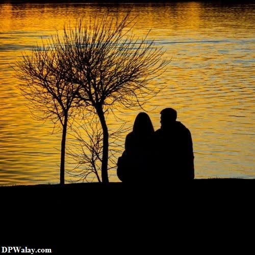 a couple sitting on the bank of a river at sunset